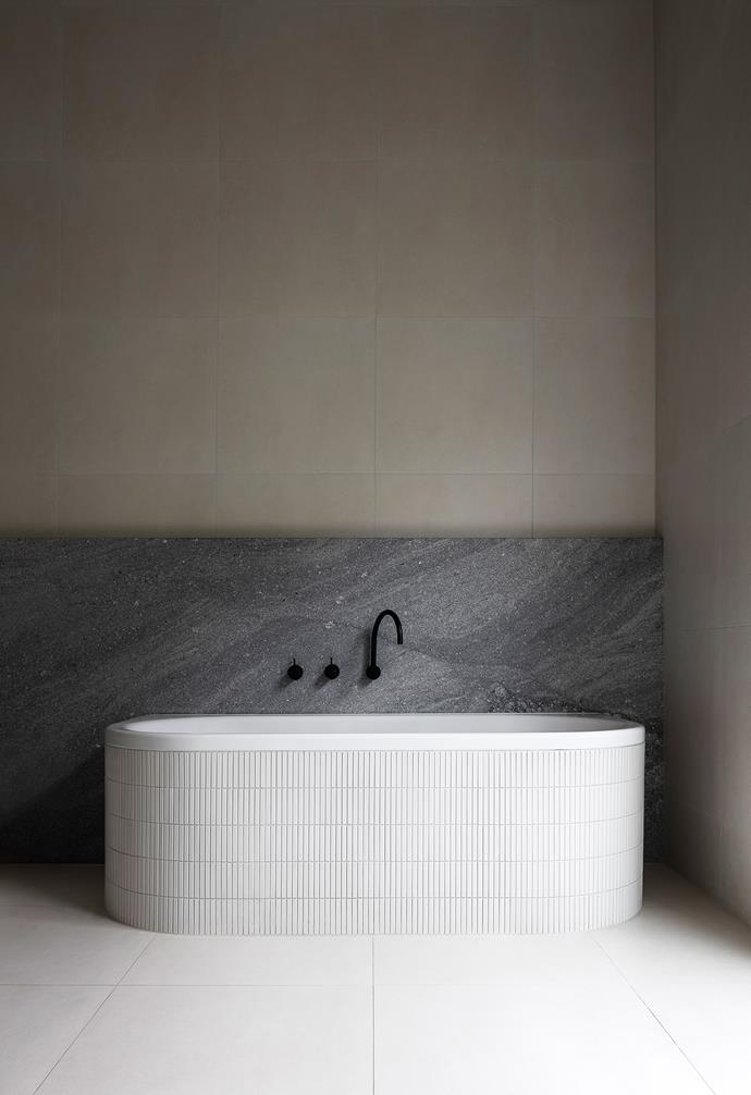 The freestanding bath has been laid with the same kitkat tiles used in the kitchen and positioned in front of the granite slab to become a sculptural centrepiece.
