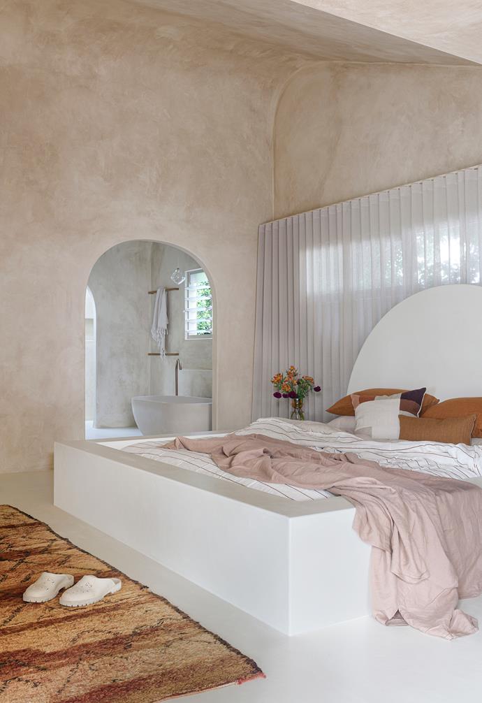 Reminiscent of a [Mediterranean haven](https://www.homestolove.com.au/mediterranean-style-houses-20407|target="_blank"), the master bedroom features an arched doorway to the ensuite and a custom built-in bed by Bradford Constructions, also rendered by Render X. The couple took an unorthodox approach to concealing the exposed ceiling beams of the original house throughout. "Our plasterers had to do a different procedure of wetting the actual plasterboard itself and to curve it and continue that line, and then Matt put render over the top of it," Emma says.