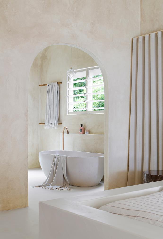 Natural light streams in through louvre windows above a [freestanding bath](https://www.homestolove.com.au/freestanding-bath-design-ideas-4520|target="_blank") from Concrete Nation. Brushed copper tapware from ABI Interiors and hand-blown glass pendants by Søktas elevate the sense of spa-inspired luxury.