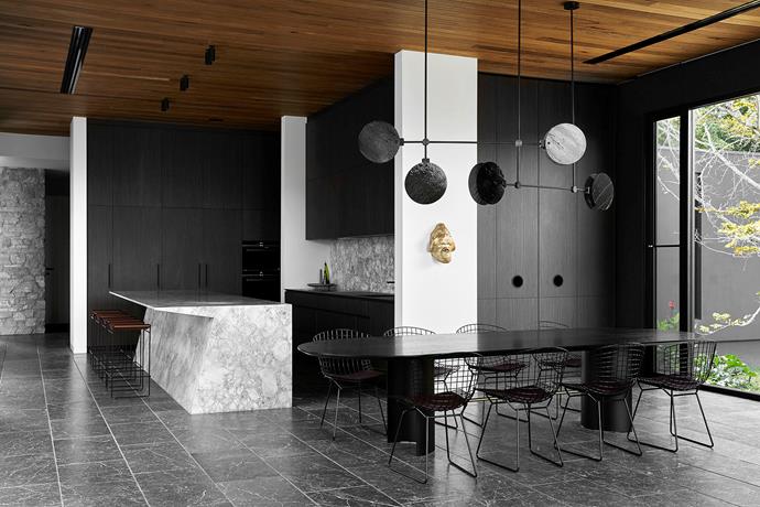 An existing wall sculpture of the client's provides a subtle, golden element to an otherwise [monochromatic kitchen](https://www.homestolove.com.au/black-and-white-kitchens-21138|target="_blank") and dining, including a custom 'Nebulae' horizontal chandelier in bubble glass and anodised frame by Ross Gardam from Stylecraft.