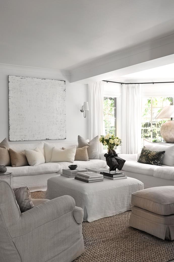 A Jenny Topfer artwork echoes the pure white palette of the home. Custom sofa in Belgian linen and custom ottoman/coffee table in washed Belgian linen. Abaca rug from International Floorcoverings.