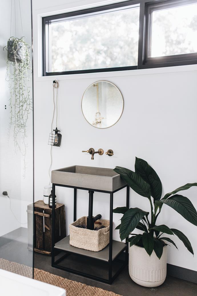 The second bathroom, lighter in palette, is decked out with a modern concrete sink and plenty of plantlife.