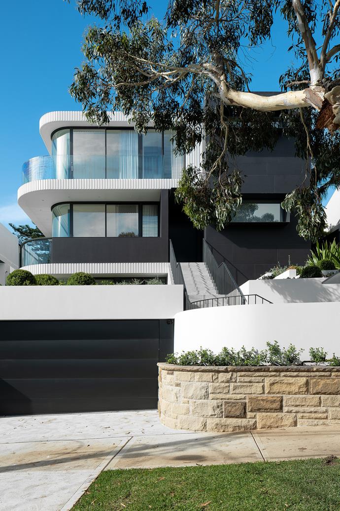 The imposing facade is a celebration of curves and fluting, framed by a long-time resident eucalypt. House clad in acrylic render, with all fluting off-form concrete. Wall cladding in Grande Max 'Basaltina' stone from Skheme. The wall colours are Dulux 'Natural White' and Dulux 'Mossman Gorge'.