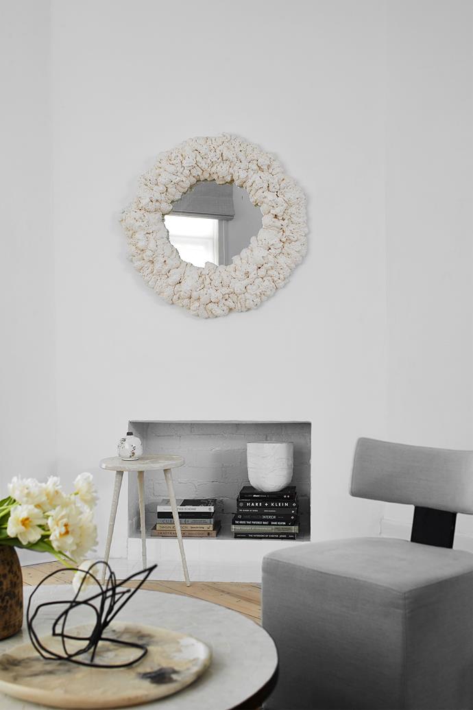 A custom-made foam-framed mirror hangs on the living area's wall, which is painted Dulux Natural White. Beige armchair from Weylandts (now closed) and small white plaster table made by Katie. Custom wire sculpture by Coton Collective and vessel on books made by Katie.