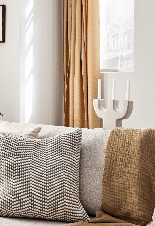 Styling your living room doesn't need to be complicated or expensive. Here, simple IKEA Moalina curtains, a Rubbleabra candle holder from Curated Spaces, the Favo cushion by Eadie Lifestyle and an Avalene throw from Papaya combine to give this space a cosy, calming update.