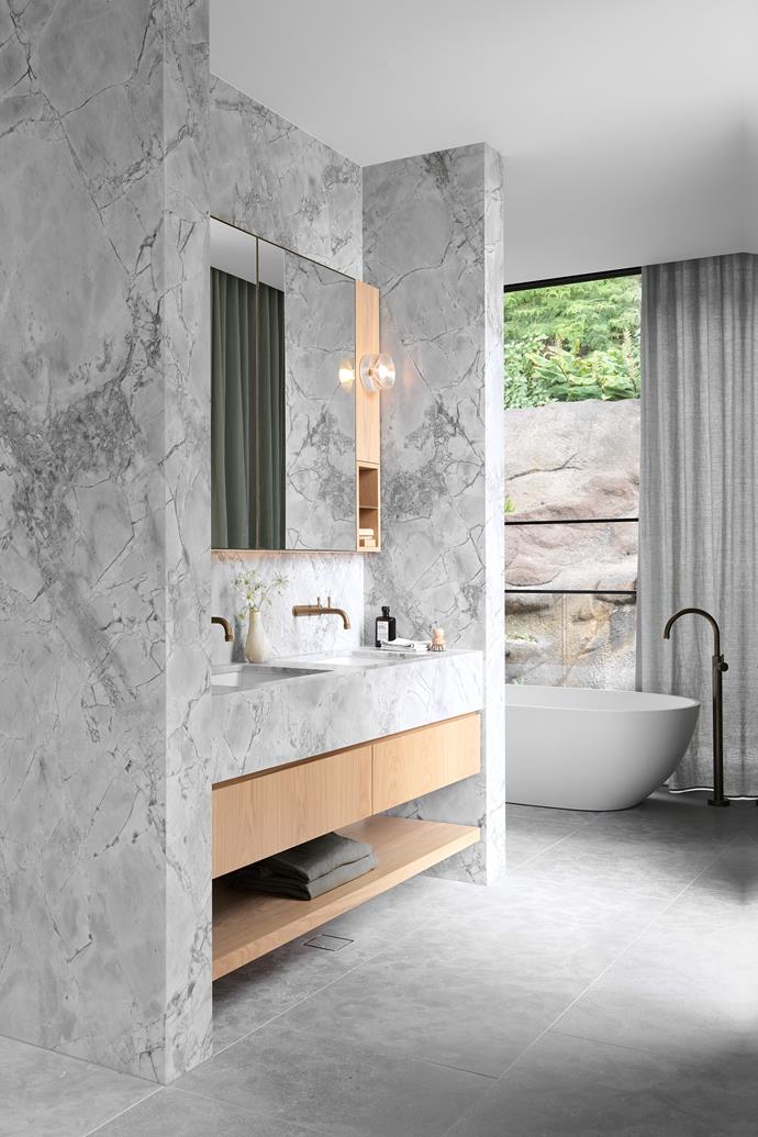 The bushland and sandstone setting offer a private outlook from the main ensuite. StoneKast 'Pebble' bath from Just Bathroomware. Solis curtain in Mint from Zepel. Benchtop and walls in Super White marble from Euro Marble. 'Yokato' brass tapware from Brodware. 'Anton' sconce from Volker Haug.
