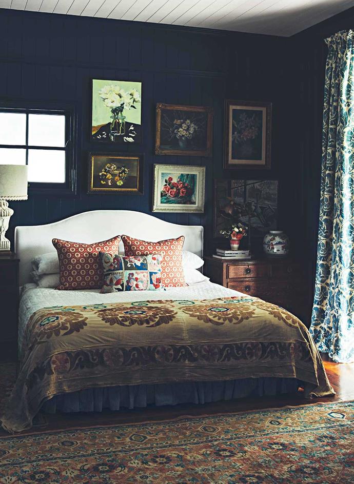 Anna's bedroom is a dark sanctuary in navy blue complemented by a white French quilt and white quilted bedhead under a collection of antique flower paintings.