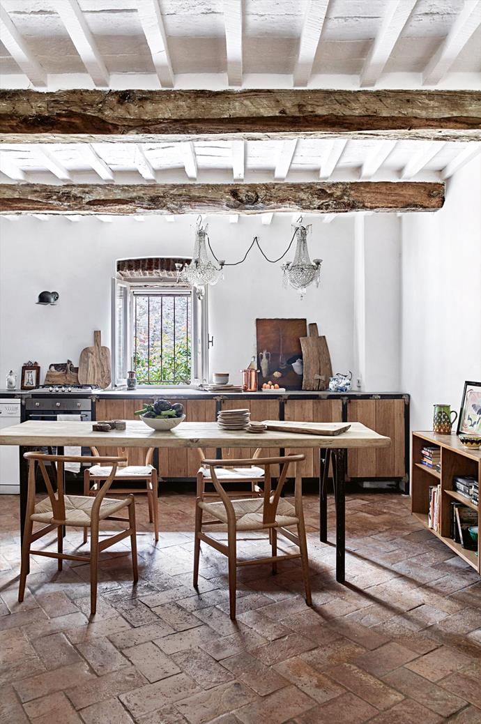 The rustic kitchen and dining room features brick floors, exposed wooden beams and a set of vintage Hans Wegner 'Wishbone' chairs.