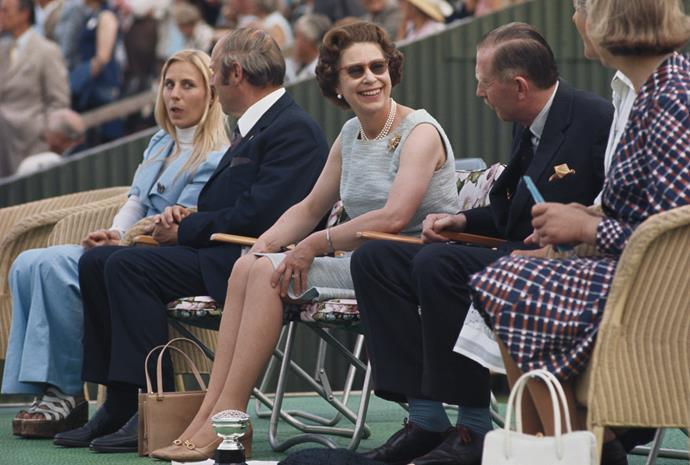 Queen Elizabeth II, wearing a chic pair of shades, turns to talk to friends while watching the polo at Smith's Lawn in Windsor, Berkshire, England, Great Britain, circa 1980.