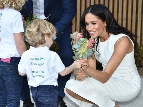 In her high heels and body-con dress - and carrying a growing bump - Meghan gets down to Findlay's level to receive a posy of Australian natives. (Images: Getty Images).