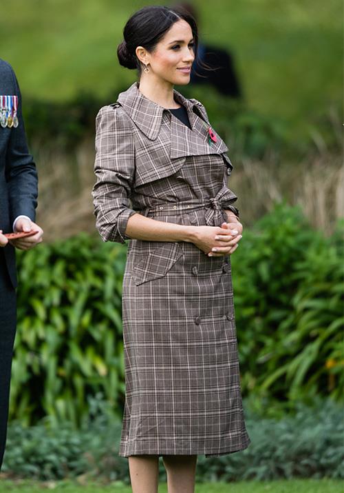 Meghan stepped off the plane in New Zealand looking radiant in a printed trench coat by Kiwi designer Karen Walker. Underneath, the Duchess wore a simple black maternity dress by ASOS. *(Image: Getty Images)*