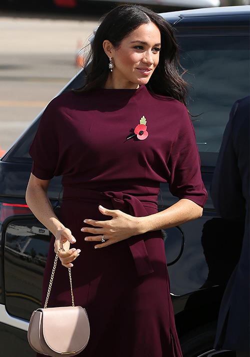 Meghan stepped out in a maroon Hugo Boss dress for her departing flight from Sydney. She paired it with a pale pink Cuyana saddle bag and some stunning pearl drop earrings.