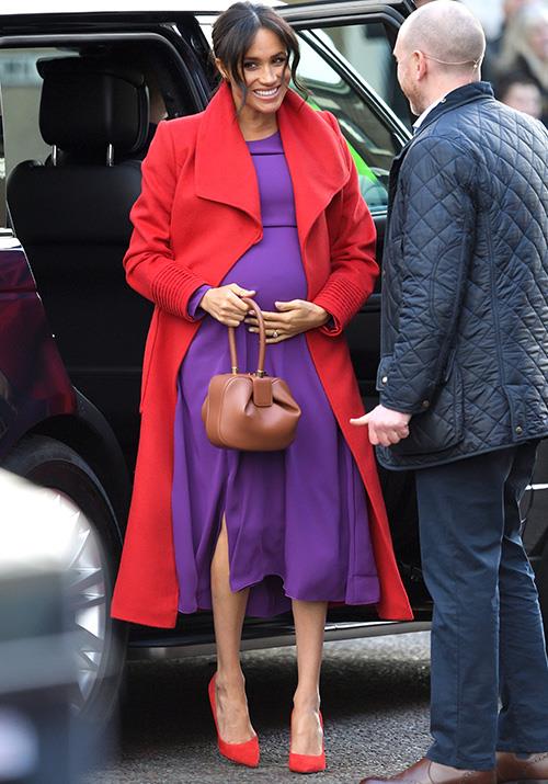 With her baby bump on show, Meghan looked stunning in purple Babaton by Aritizia dress paired with a red wrap coat by designer Sentaler. *(Image: Getty Images)*