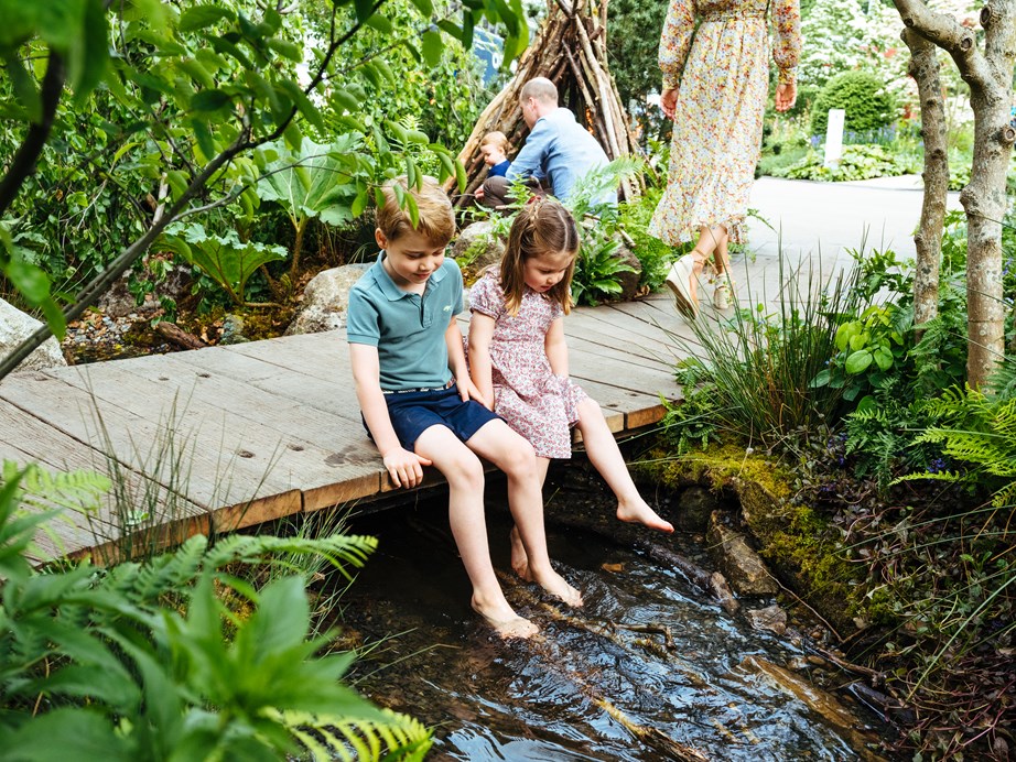 Prince George and Princess Charlotte dangle their feet in the stream. *(Image: Matt Porteous / Getty)*