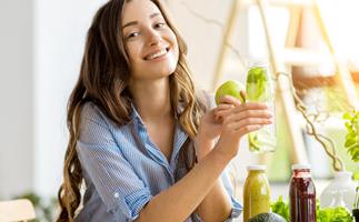 Happy woman sits at table with green vegetables and juices