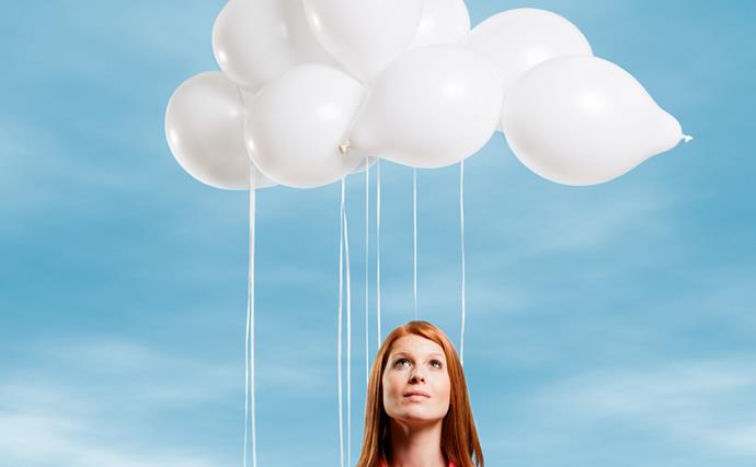Red-headed woman looking up to sky white balloons forming clouds