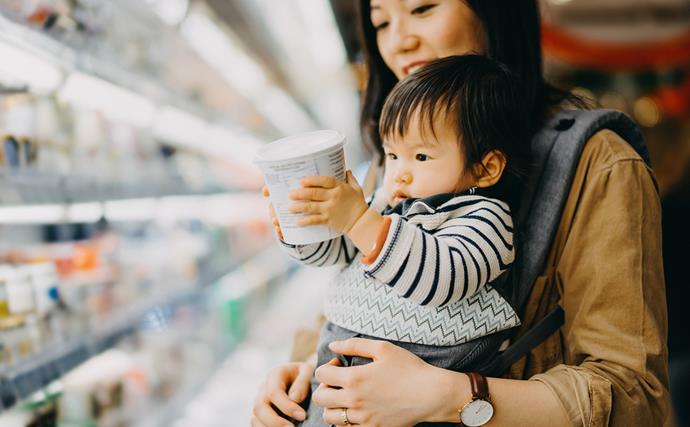 baby holding yoghurt tub in supermarket with mum