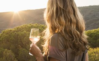 Woman holding glass of wine watching sunset over hills