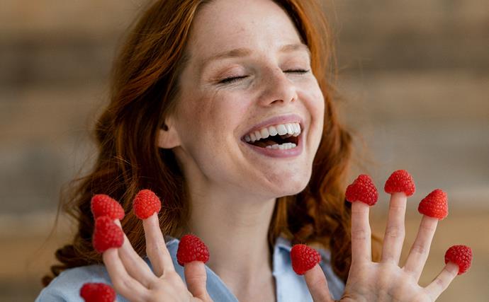  laughing redheaded woman with raspberries on her fingertips
